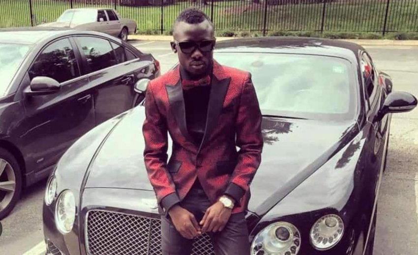 A man wearing sunglasses and a red suit sitting on the hood of a car.